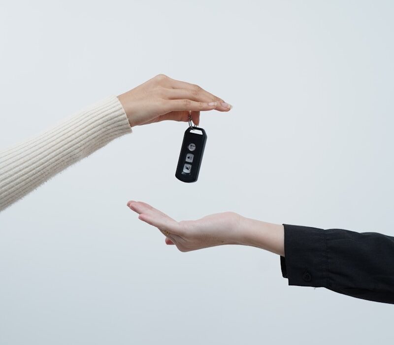 Hands exchanging car keys against a white background.